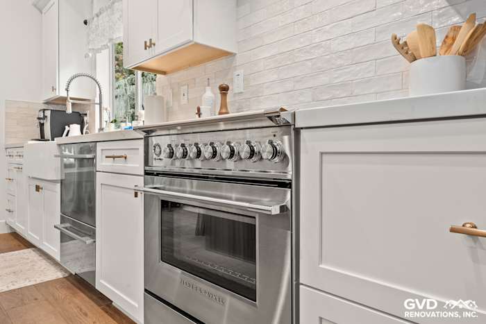 Sleek white Waypoint cabinets with mitered Vadara Bronzo countertops and stainless steel range in Folsom kitchen remodel