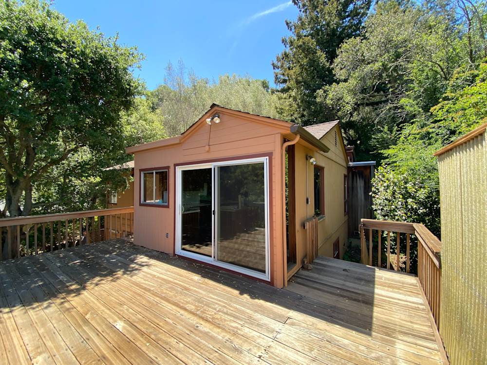 Wood deck leading to a light-colored exterior cabin surrounded by greenery in Northern California