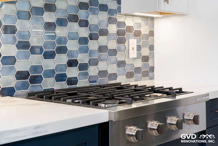 Hexagon mosaic backsplash in blue tones behind a modern gas stove with stainless steel features