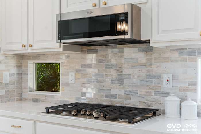 Modern kitchen featuring a stainless steel microwave above a gas stove, glass tile backsplash, and white cabinetry