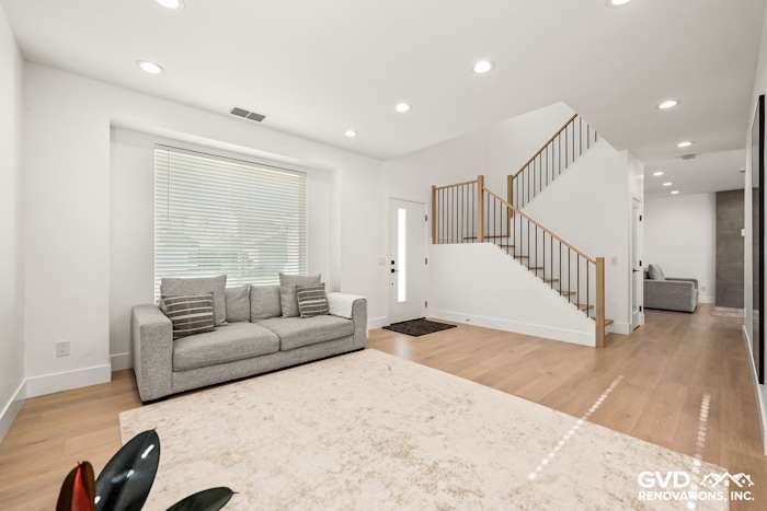 Bright entryway featuring a modern staircase, large windows, and stylish gray sofa with light hardwood flooring