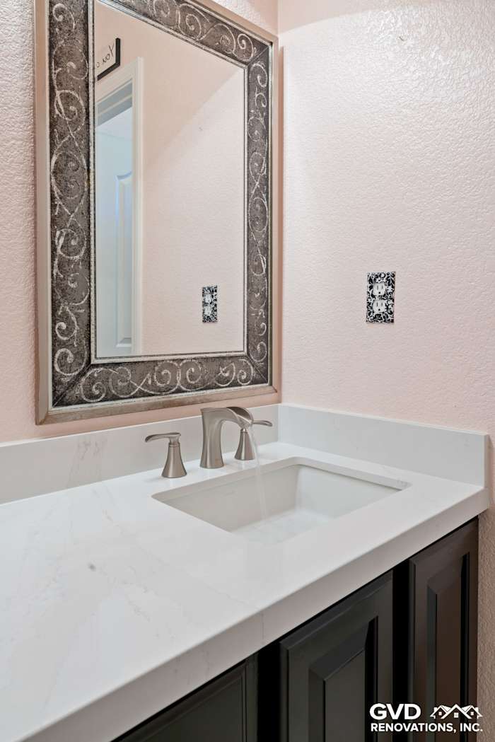 Modern bathroom vanity with a white quartz countertop, dark cabinetry, and decorative mirror