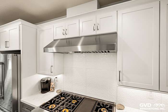 Modern kitchen with white cabinets, stainless steel hood, quartz countertops, and decorative backsplash in Folsom, CA