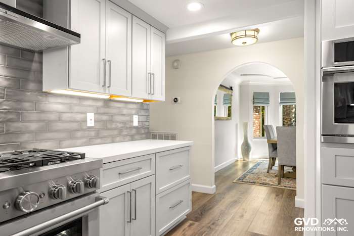 Modern kitchen featuring white cabinets, gray subway tile backsplash, stainless steel appliances, and warm wood flooring