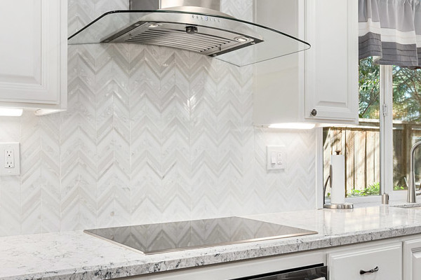 Modern kitchen remodel featuring white cabinetry, herringbone tiled backsplash, quartz countertops, and hardwood flooring