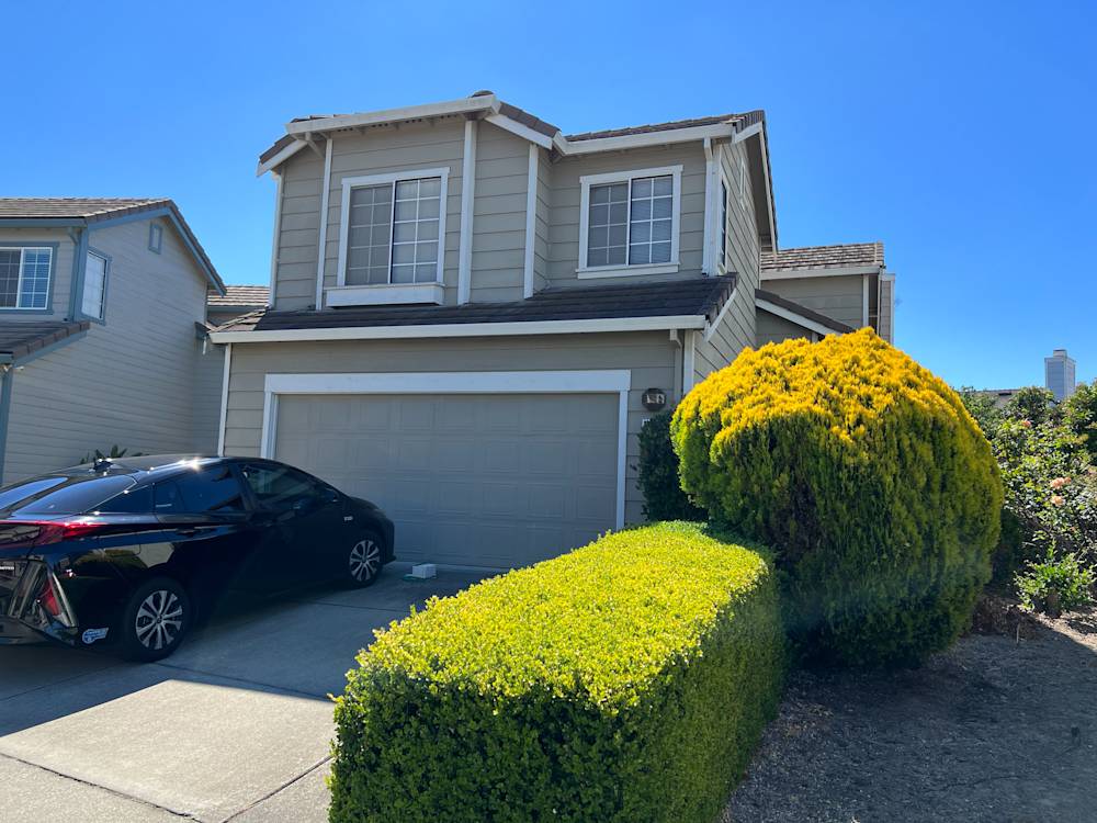 Curb view of a two-story home in Sacramento with manicured hedges and a dark car in driveway