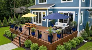 Spacious outdoor deck with seating, umbrellas, and potted plants next to a blue house in a serene backyard