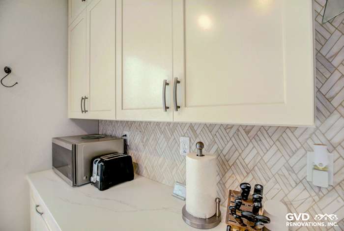 Modern kitchen remodel in Roseville featuring herringbone tile backsplash, white cabinetry, and countertop appliances