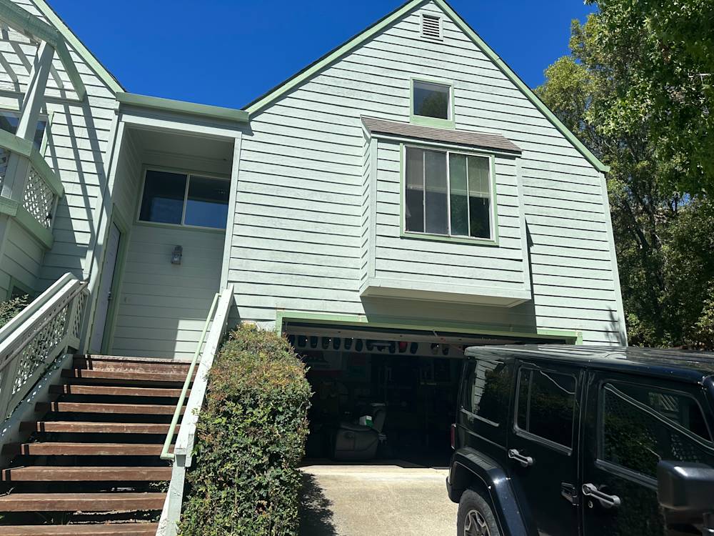 Green clapboard house with large front window and wooden stairs in Sacramento