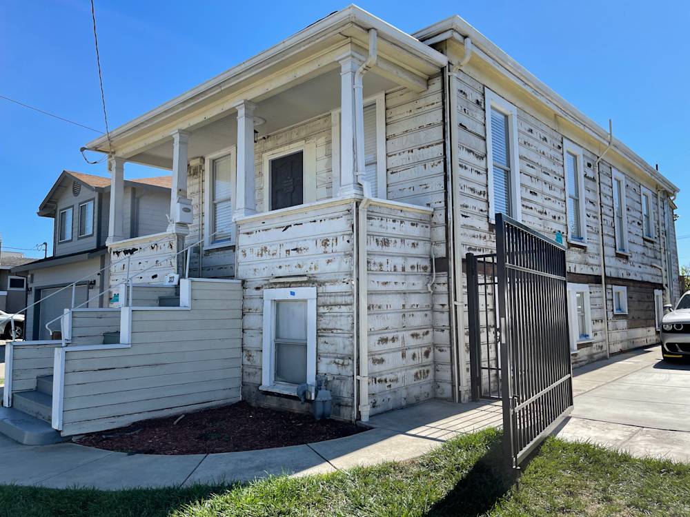 Weathered house exterior with peeling paint and concrete walkway in Sacramento