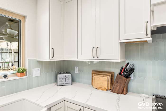 Light gray kitchen countertop with white cabinets, hexagon backsplash, and wooden cutting boards in Carmichael remodel