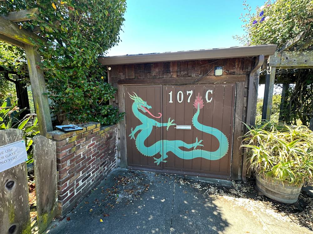 Rustic wooden gate with a colorful dragon mural in Sacramento, surrounded by greenery and brick wall