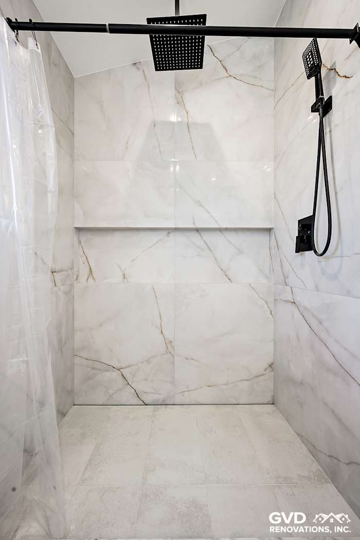 Modern bathroom shower with large white marble tiles, sleek black fixtures, and a frameless glass door