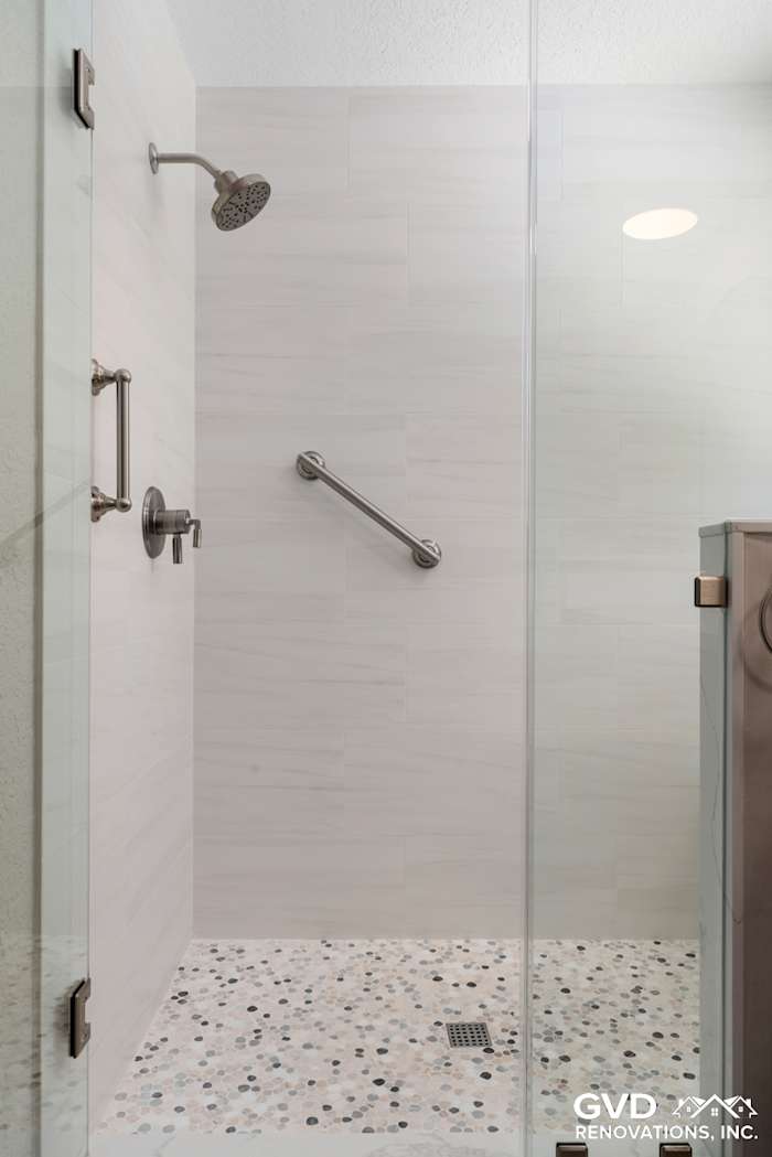 Modern walk-in shower featuring a textured stone floor, grab bar, and sleek glass enclosure
