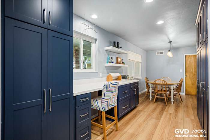 Modern kitchen with navy blue cabinetry, light wood flooring, and a dining area, featuring a stylish bar stool