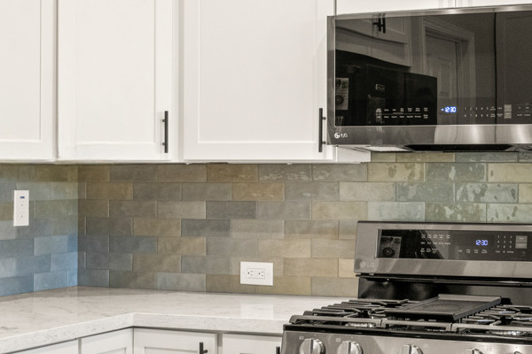 Modern kitchen remodel with white shaker cabinets, quartz countertops, black appliances, and glass tile backsplash
