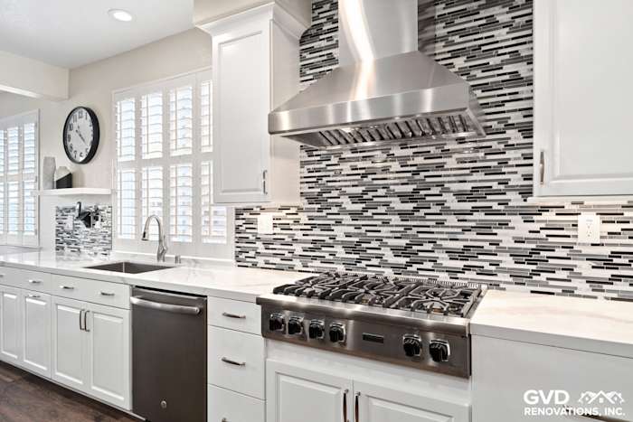 Modern kitchen with white cabinetry, sleek stainless steel appliances, and a black and gray mosaic tile backsplash