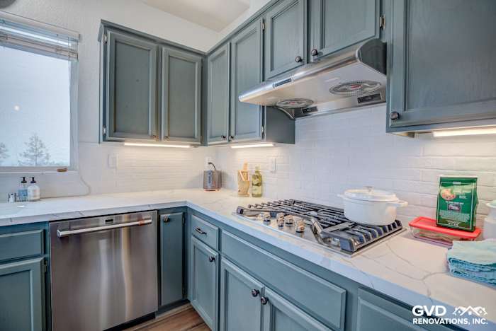 Modern kitchen with teal cabinets, quartz countertop, stainless steel appliances, and white subway tile backsplash
