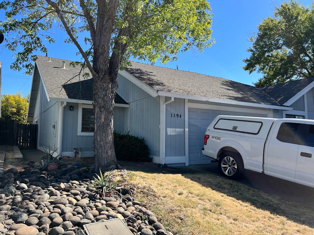 Worn home exterior with faded blue siding and unkempt landscaping in Sacramento