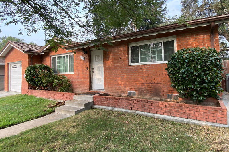 Dated red brick exterior with overgrown shrubs and cracked walkway