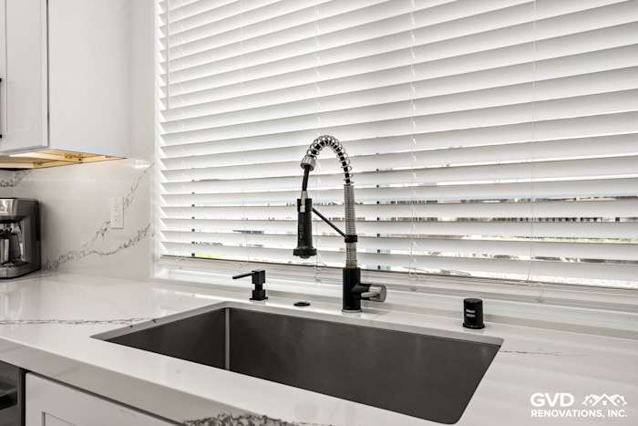 Quartz countertop with a modern sink and stylish faucet beneath window blinds in a kitchen remodel