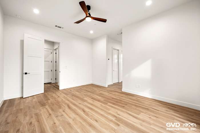 Bright, spacious bedroom with light wood flooring, white walls, and modern ceiling fan in new construction home