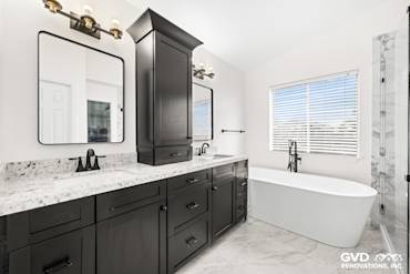 Modern bathroom with a double sink vanity, black cabinetry, freestanding tub, and large windows