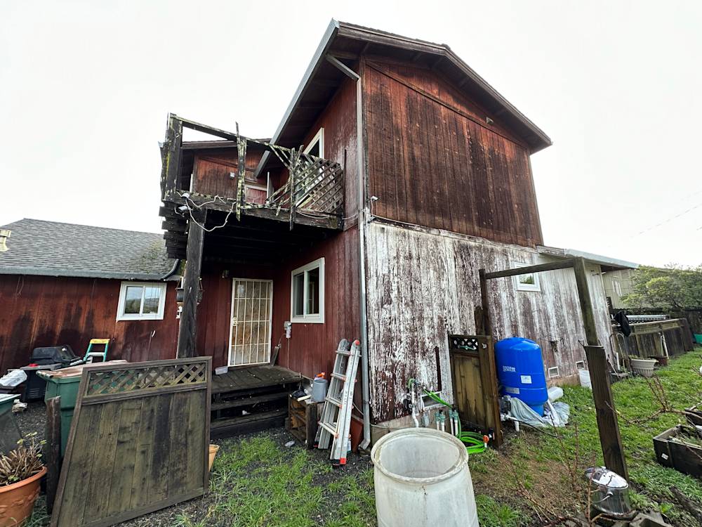 Weathered red wood siding on two-story home in Sacramento, cluttered yard with gardening tools and equipment