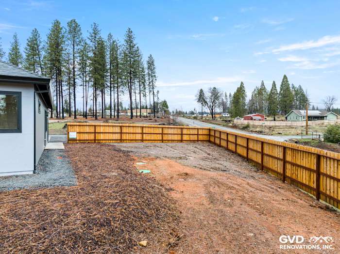New home exterior in Paradise, CA featuring wooden fence, gravel landscaping, and surrounding pine trees
