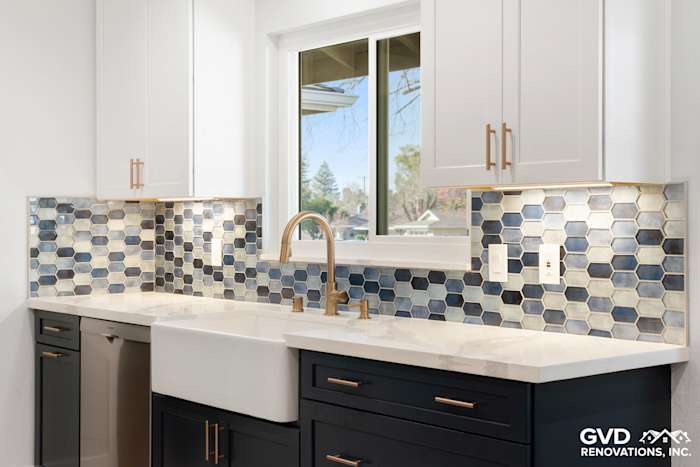 Stylish kitchen backsplash with hexagon tile in blue and gray, featuring a farmhouse sink and gold faucet