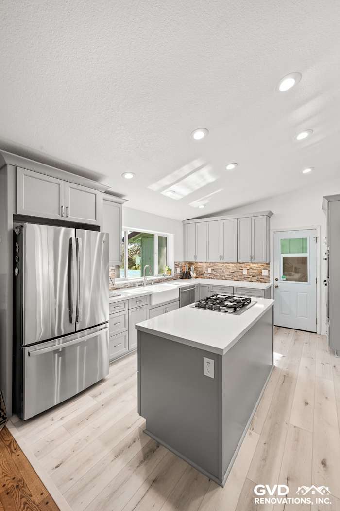 Modern kitchen remodel featuring gray cabinetry, quartz countertop island, stainless steel appliances, and bright lighting