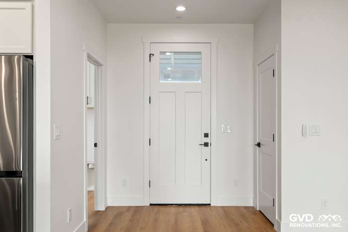 Bright entryway featuring a white paneled front door, light hardwood flooring, and modern trim details