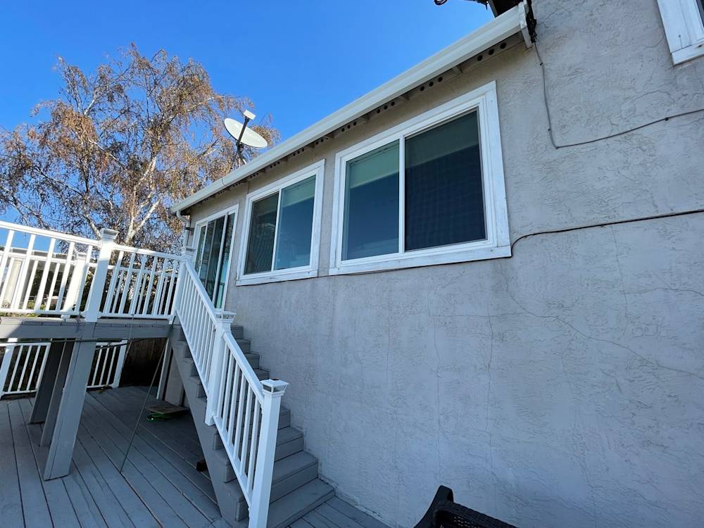 Old gray stucco exterior with white trim and wooden deck in Sacramento