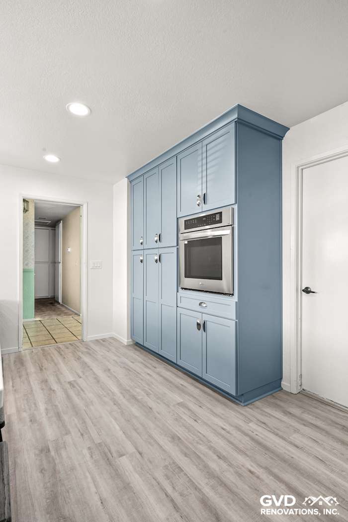 Modern kitchen featuring blue Waypoint cabinets, built-in oven, and light wood flooring in Elk Grove