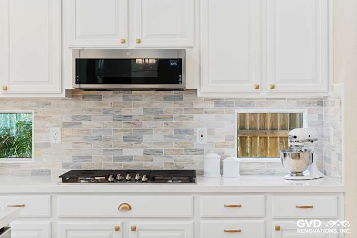 Renovated kitchen with white cabinetry, marble backsplash, built-in microwave, and stainless-steel appliances