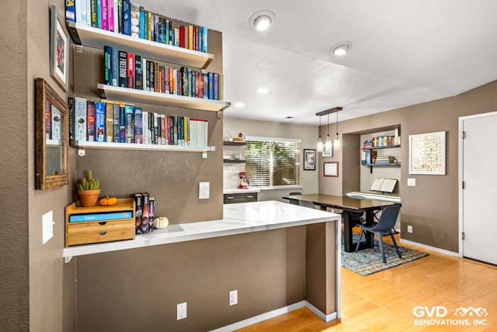 Modern kitchen with quartz countertop, open shelving, and seating area, featuring warm brown walls and natural light