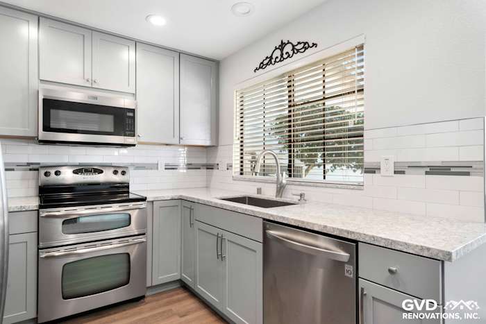 Modern kitchen featuring gray cabinets, stainless steel appliances, quartz countertops, and subway tile backsplash