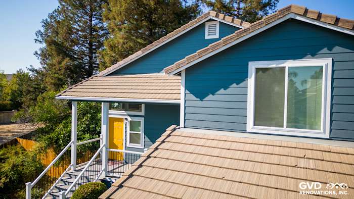 Updated home exterior in Dixon, showcasing new blue siding, beige roofing, and a vibrant yellow front door
