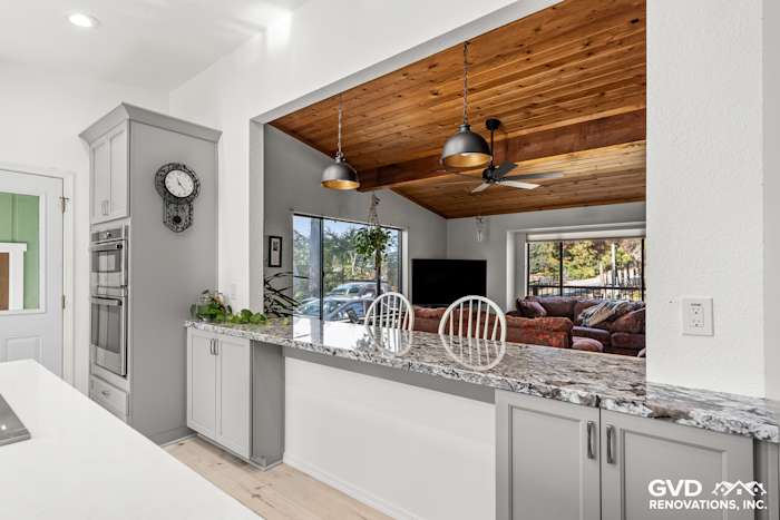 Modern kitchen remodel featuring gray cabinetry, granite countertop, open layout, and wooden ceiling accents