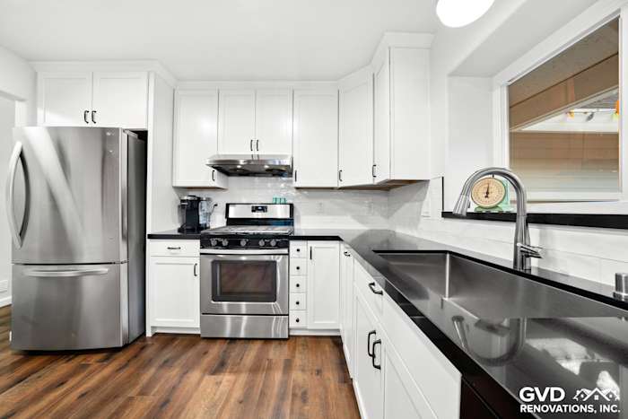 Modern white shaker kitchen featuring stainless steel appliances, quartz countertops, and dark wood flooring