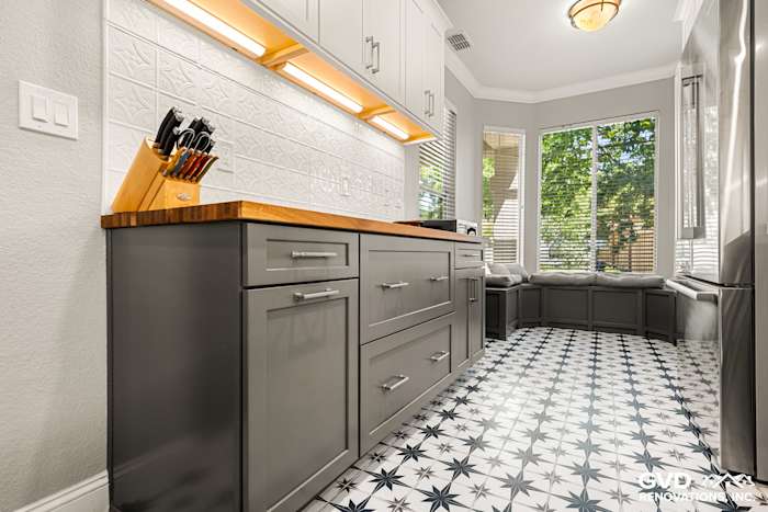 Modern kitchen remodel featuring gray cabinets, patterned black and white tile flooring, and a wooden countertop