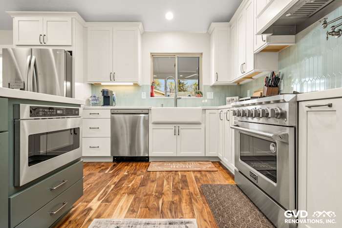 Modern kitchen remodel featuring custom white cabinets, stainless steel appliances, farmhouse sink, and warm wood flooring