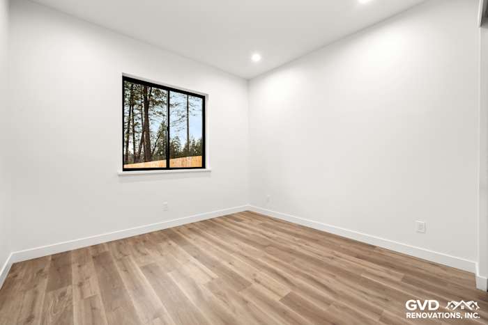 Bright bedroom featuring large window, modern trim, and warm wood flooring in new construction home in Paradise, CA