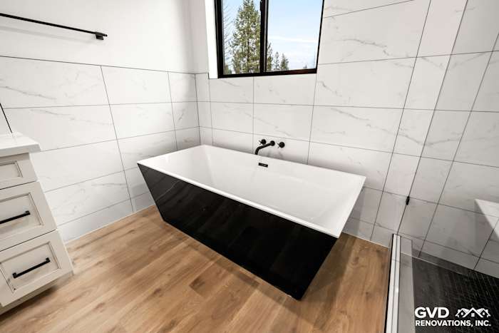Modern bathroom in Paradise, CA featuring a sleek black bathtub against marble wall tiles and wood flooring