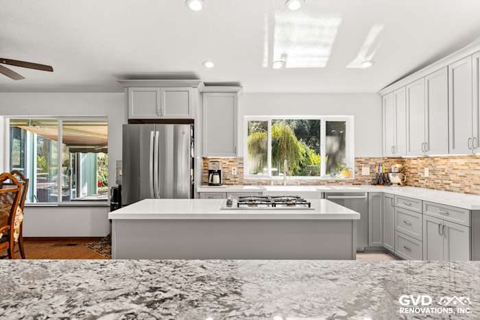 Modern kitchen remodel featuring gray cabinetry, quartz island, and mosaic backsplash with natural light