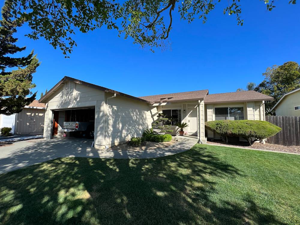 Single-story home in Sacramento with a green lawn, concrete driveway, and shaded porch area
