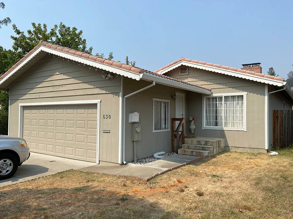 Worn beige siding with outdated roof, overgrown grass, and faded windows