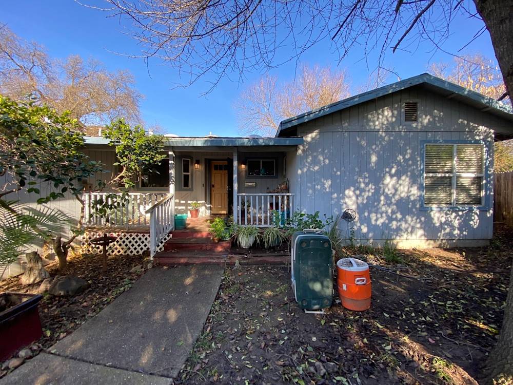 Dilapidated exterior of a home in Sacramento with overgrown landscaping and worn steps