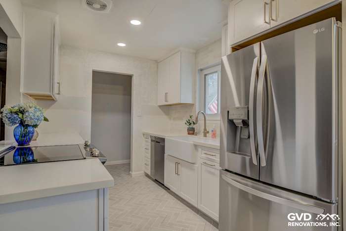 Modern kitchen with white cabinetry, quartz countertops, stainless steel appliances, and herringbone tile flooring