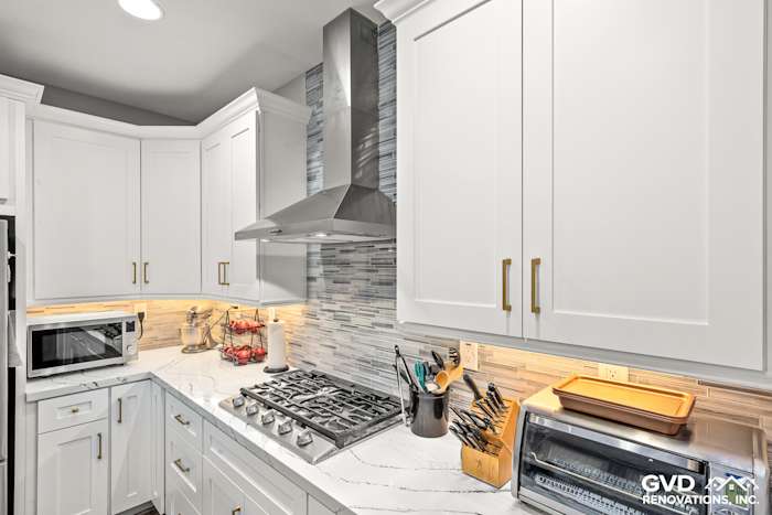 Modern kitchen with white custom cabinets, Cambria countertops, and stylish backsplash featuring a stainless steel range hood
